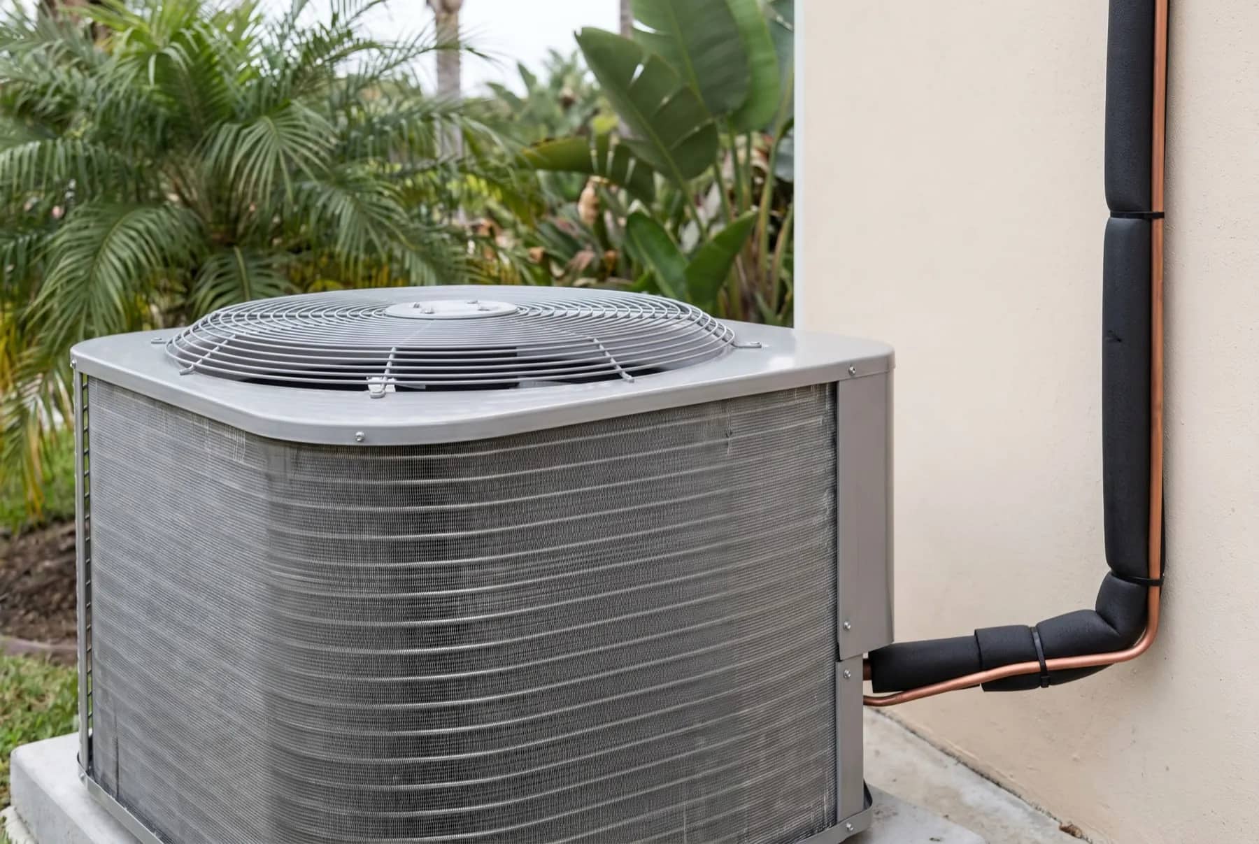 Residential air conditioning condenser unit on a concrete pad beside a stucco wall