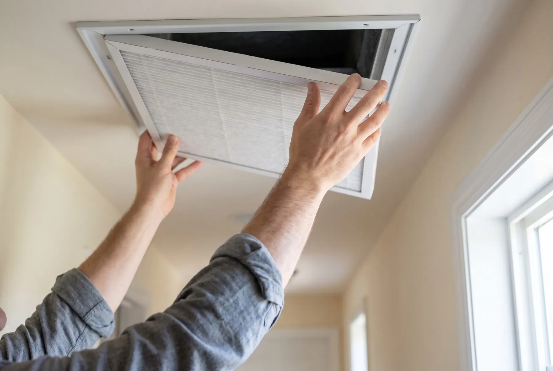 Hands sliding a clean pleated air filter into a ceiling return air grille